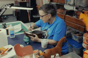 Nichole Leavy sites at a desk working on her her art, painting the inside of a box